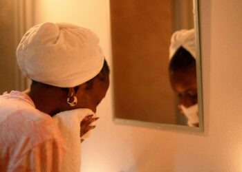 Woman with a towel wrapped around her hair drying her face in front of a mirror